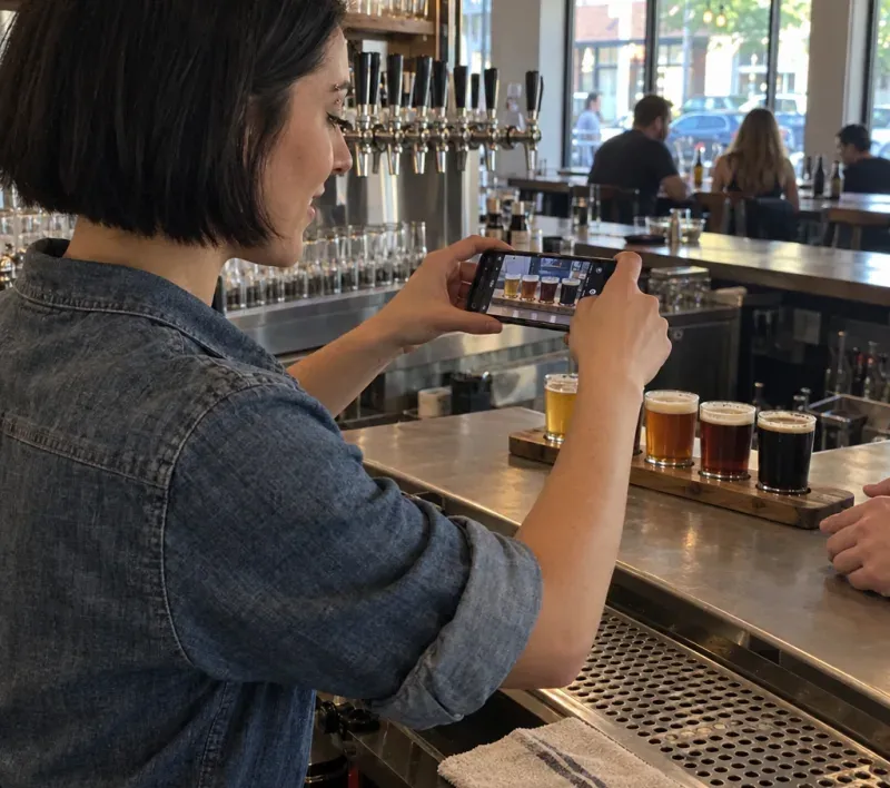 A bartender photographing a tasting paddle of four beers with her phone before serving it