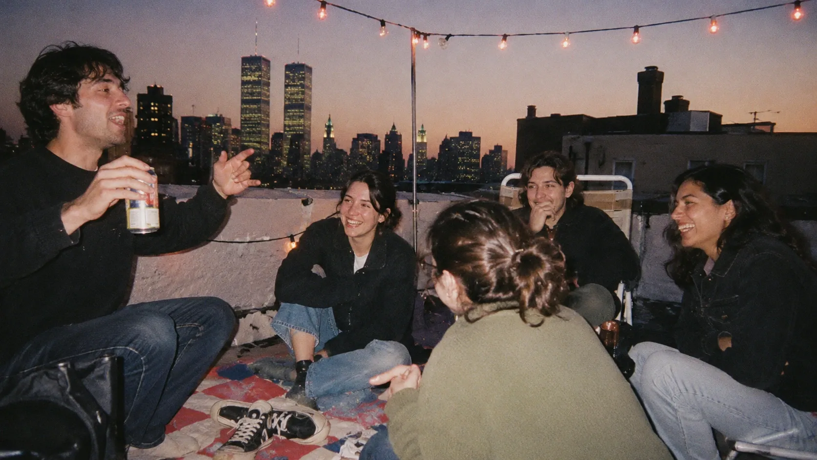 Young friends laughing together on a rooftop at dusk under string lights