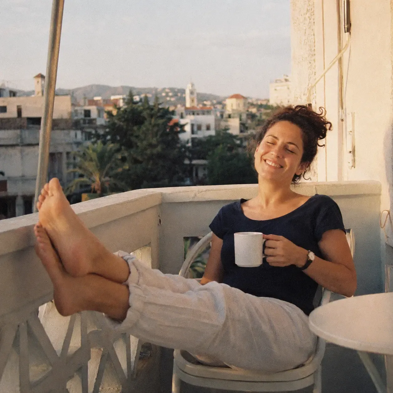 A happy person relaxing on a sunlit balcony, coffee in hand, no screens